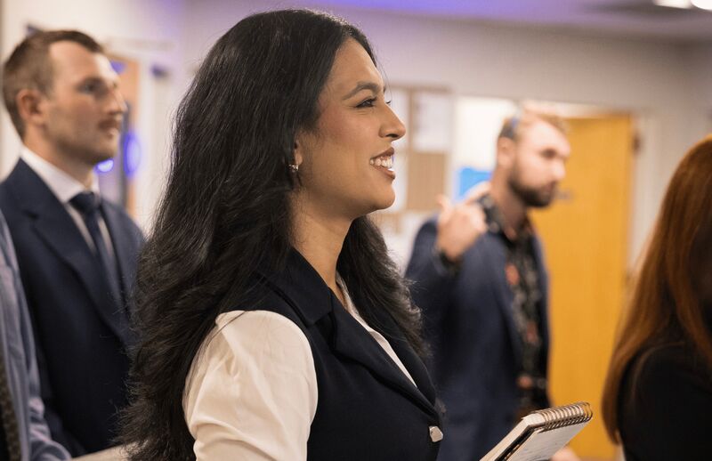 A smiling Palmora team member with her notebook among colleagues at the morning meeting