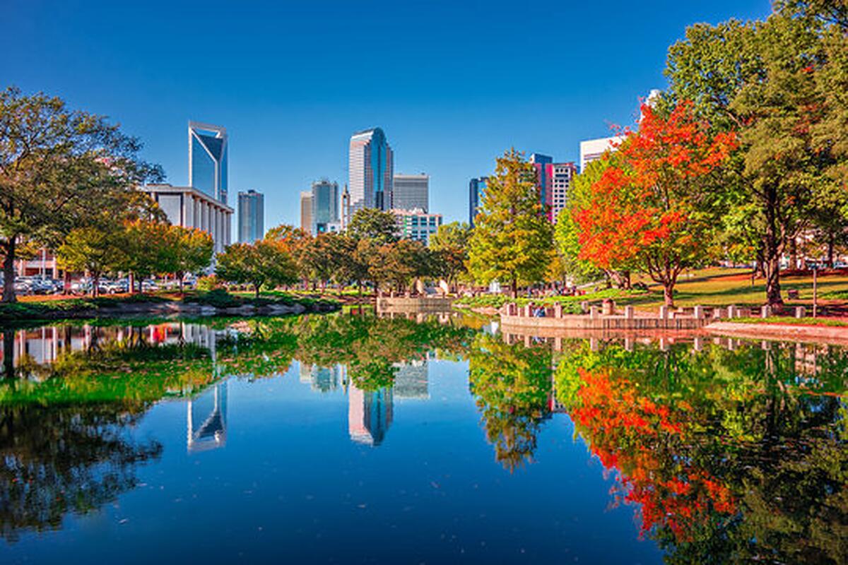 The Charlotte skyline reflected in a city-park lake among autumn trees